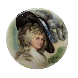 Puede incluir: Retrato en miniatura redondo, pintado a mano, de una mujer con sombrero negro con ribete blanco y vestido blanco. La mujer tiene cabello rubio rizado y una expresión serena. El texto dice "Gainsborough by Joh. Peter Amsterdam Holland".