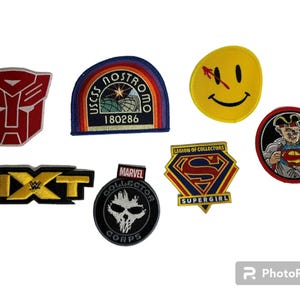 May include: Collection of embroidered patches featuring various designs. Includes a red and white Transformers logo, a USS Nostromo patch, a yellow smiley face, a Superman patch, a Marvel Collector Corps patch, a Supergirl patch, and an NXT patch.