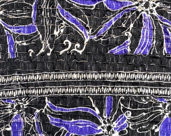 Könnte beinhalten: Nahaufnahme eines schwarzen Stoffes mit floralem Muster. Das Design zeigt große, stilisierte Blumen in Lila- und Weißtönen auf schwarzem Hintergrund. Der Stoff hat ein strukturiertes, geripptes Aussehen mit einem horizontalen weißen Streifen.