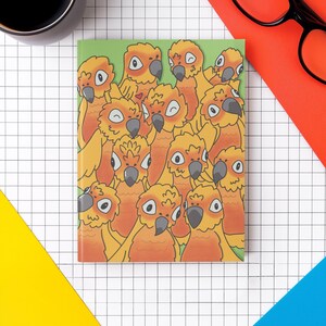 May include: A notebook with a green background featuring a cartoon illustration of multiple orange and yellow parrots. The notebook is surrounded by a black coffee mug, black glasses, and colorful geometric shapes on a white grid.