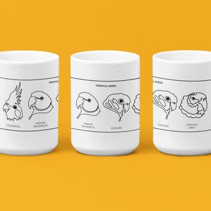 Könnte beinhalten: Drei weiße Keramikbecher mit schwarzen Strichzeichnungen von tropischen Vögeln. Jeder Becher zeigt ein anderes Vogeldesign, darunter ein Kakadu, ein Halsbandsittich und ein Conure. Auf den Bechern steht "TROPICAL BIRDS".