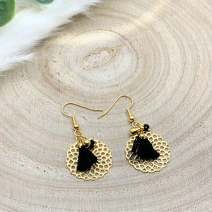 Peut inclure: Une paire de boucles d'oreilles dorées avec des breloques en forme de pompons noirs et un motif délicat en filigrane circulaire.
