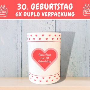 K&ouml;nnte beinhalten: Wei&szlig;e zylindrische Kerze mit roten Herzen und dem Text "Alles Gute zum 30 Geburtstag" in einem roten Herzen.