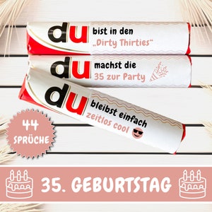 May include: Three white chocolate bars with red and black accents. The bars have different sayings on them, including "du bist in den "Dirty Thirties"", "du machst die 35 zur Party", and "du bleibst einfach zeitlos cool". A pink circle with the text "44 SPRÜCHE" is in the lower left corner. A pink banner with the text "35. GEBURTSTAG" and a white cake icon is at the bottom of the image.