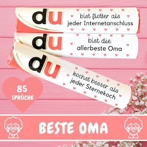 May include: Three pink and white candy bars with the word "du" printed on them. Each bar has a different message printed on it, including "bist flotter als jeder Internetanschluss", "bist die allerbeste Oma", and "kochst besser als jeder Sternekoch". The bars are arranged vertically with the top bar partially obscured by the bar below it. The bars are on a pink wooden surface. The text "85 SPRÜCHE" is printed in a heart shape below the bars. The text "BESTE OMA" is printed in a banner below the heart. Two cartoon images of a person with glasses and curly hair are on either side of the banner.