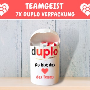 May include: White cylindrical container with a red heart and the text "Du bist das des Teams" (You are the one of the team). The container is filled with red and white Duplo building blocks. The container has the word "Duplo" printed on the side.