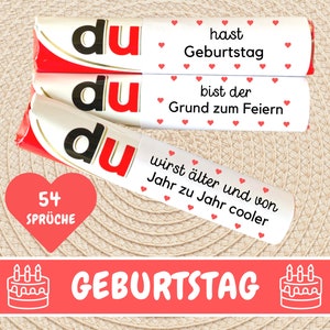 Puede incluir: Tres barras de chocolate blanco con envoltorios rojo y blanco. Los envoltorios tienen la palabra "du" impresa en negro. El texto en los envoltorios dice "hast Geburtstag", "bist der Grund zum Feiern" y "wirst älter und von Jahr zu Jahr cooler". Un corazón rojo con el texto "54 Sprüche" está en la esquina inferior izquierda. Una pancarta roja con el texto "GEBURTSTAG" y un contorno blanco de un pastel de cumpleaños con velas está en el centro inferior.