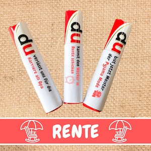 May include: Three red and white tubes with the word "du" printed on them. The tubes have different messages printed on them, including "bist jetzt Meister der Pyjama Mode", "kannst den Wecker in Rente schicken", and "verl&auml;sst uns f&uuml;r die Karriere als Opa". The tubes are sitting on a brown burlap surface. The text "RENTE" is printed in white on a red background below the tubes.