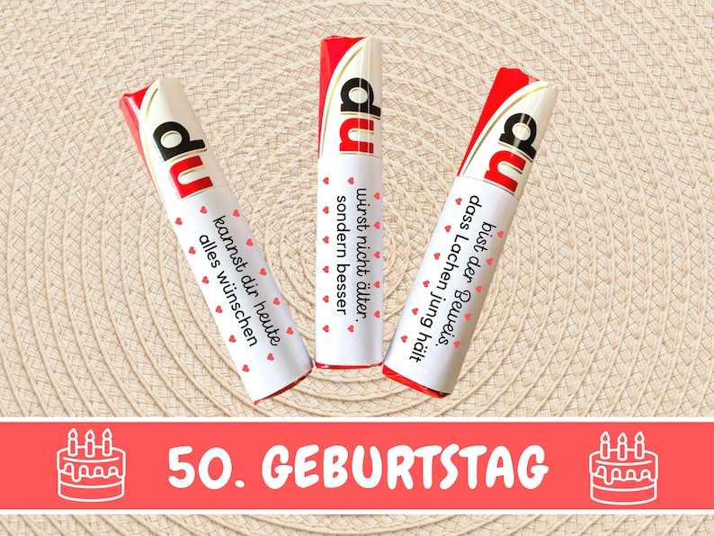 May include: Three red and white candy bars with the word "du" printed on them. Each bar has a different message printed on it. The bars are arranged in a semi-circle on a woven straw-like surface. The text below the bars reads "50. GEBURTSTAG" with a cake icon on either side.