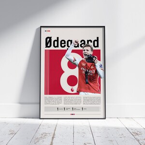 May include: A retro-style poster featuring a soccer player in a red and white jersey with the number 8 on the front. The player is raising his right arm in celebration. The poster has the text "Ødegaard" at the top and "1 1 1 1" at the bottom.