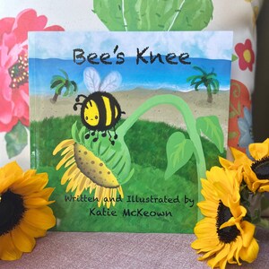 May include: A children's book cover with a yellow and black bee on a sunflower. The book title is "Bee's Knee" and the author is Katie McKeown.