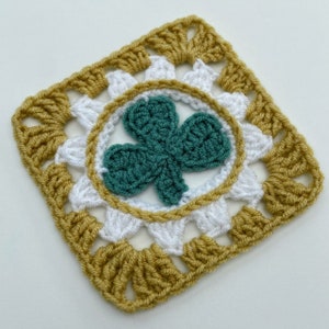 May include: A square, crocheted item featuring a green shamrock in the center, surrounded by a white circle and a gold border. The outer edges are gold, with white squares in between. This handmade item is perfect for St. Patrick's Day.