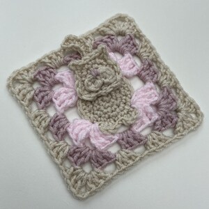 May include: A crocheted square with a pink and beige color scheme. The square features a smaller crocheted flower in the center.