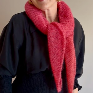 Peut inclure: Une femme porte une écharpe rose vif et duveteuse autour du cou. L'écharpe contraste avec son chemisier noir. Elle porte également des boucles d'oreilles dorées. L'écharpe semble être faite d'une matière douce et texturée.