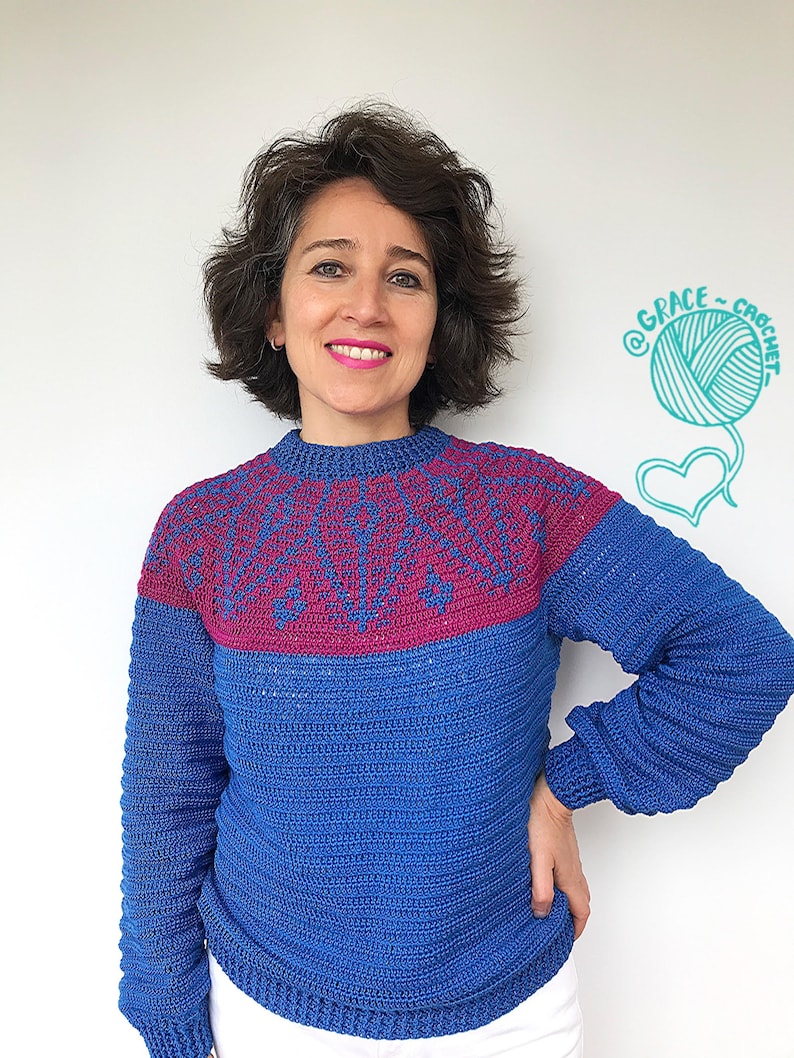 May include: A woman wearing a blue and pink crocheted sweater with a white background. The sweater has a geometric pattern on the top and a solid blue color on the bottom. The background has a drawing of a ball of yarn and a heart with the text "@GRACE_CROCHET".