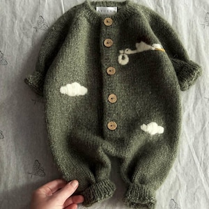 Op de afbeelding: Een groene gebreide baby romper met witte wolk en vogel applicaties en houten knopen. De romper heeft de tekst "AYUEVA" op de rug.