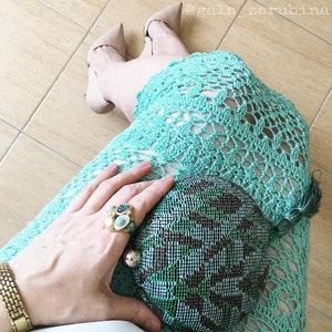 May include: A woman wearing a light blue crochet dress and nude heels holds a green and black mesh clutch. She is wearing a gold ring with colorful stones.