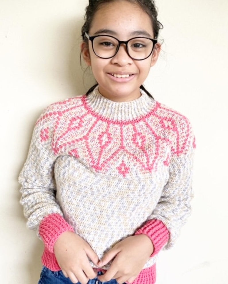 May include: A white and pink knitted sweater with a geometric pattern on the neckline and pink cuffs. The sweater has a speckled texture.