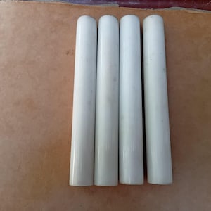 May include: Four white ceramic tubes, likely for use in a lighting fixture.