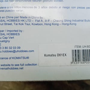 May include: A white box with black text and a barcode. The text reads "Komatsu D61EX" and "ITEM: UH 8000U". The box is for a toy construction vehicle.