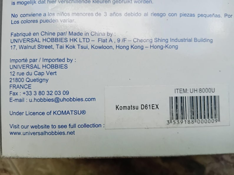 May include: A white box with black text and a barcode. The text reads "Komatsu D61EX" and "ITEM: UH 8000U". The box is for a toy construction vehicle.