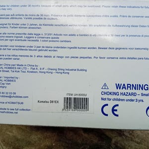 May include: A white box with blue text and a warning label. The box is for a Komatsu D61EX toy construction vehicle. The warning label reads "WARNING: CHOKING HAZARD - Small parts. Not for children under 3 yrs." The box also has a CE mark.