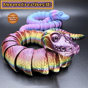 Può includere: Due serpenti stampati in 3D, uno color arcobaleno e l'altro in tonalità di blu e viola. Il serpente arcobaleno è arrotolato in un cerchio, mentre il serpente blu e viola è avvolto in una spirale sciolta. I serpenti sono realizzati da MorenoCreatives3D e sono venditori autorizzati di MatMire Makes.