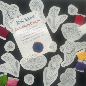 May include: A set of embroidery designs featuring various floral and plant motifs, including a flower, a pitcher plant, and a bee. The designs are printed on white paper and are accompanied by spools of embroidery floss in various colors, including red, green, yellow, and purple. The text "Stick & Stich Embroidery Designs" is printed on a white card.