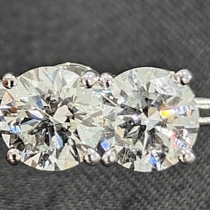 May include: Two round, clear, sparkling diamonds set in a silver band. The diamonds are set close together and are surrounded by small, silver prongs.