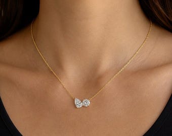 May include: A delicate gold chain necklace featuring two clear, faceted stones as a pendant. One stone is pear-shaped and the other is round, both set side-by-side on a thin, polished yellow gold cable chain that rests against the collarbone area.