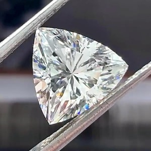 Pu&ograve; includere: Un diamante a taglio brillante, di forma triangolare, tenuto da pinzette d'argento. La gemma ha molte sfaccettature, che riflettono la luce e creano un effetto scintillante. Il diamante ha una forma triangolare.