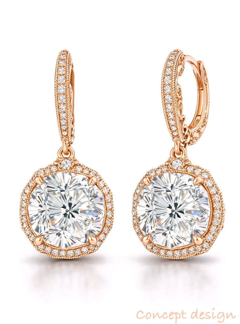 May include: A pair of rose gold earrings with a large, round, clear gemstone center, surrounded by smaller, clear stones. The earrings have a hinged hoop design and are set against a white background. The words "concept design" are in the bottom right corner.