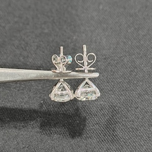 May include: A pair of silver-toned stud earrings featuring round, faceted clear stones set in a four-prong basket setting. The earrings include butterfly-style friction backs with a heart-shaped wire design, held together by metal tweezers.