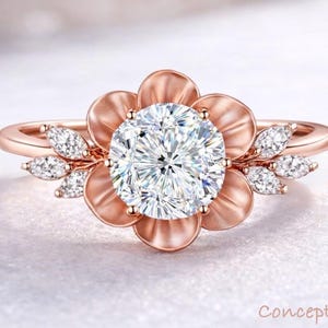 May include: Rose gold ring featuring a large, round, clear gemstone at the center, surrounded by a flower-shaped setting. Small, clear gemstones accent the petals. The ring band is also rose gold. The words "Concept design" are in the bottom right corner.