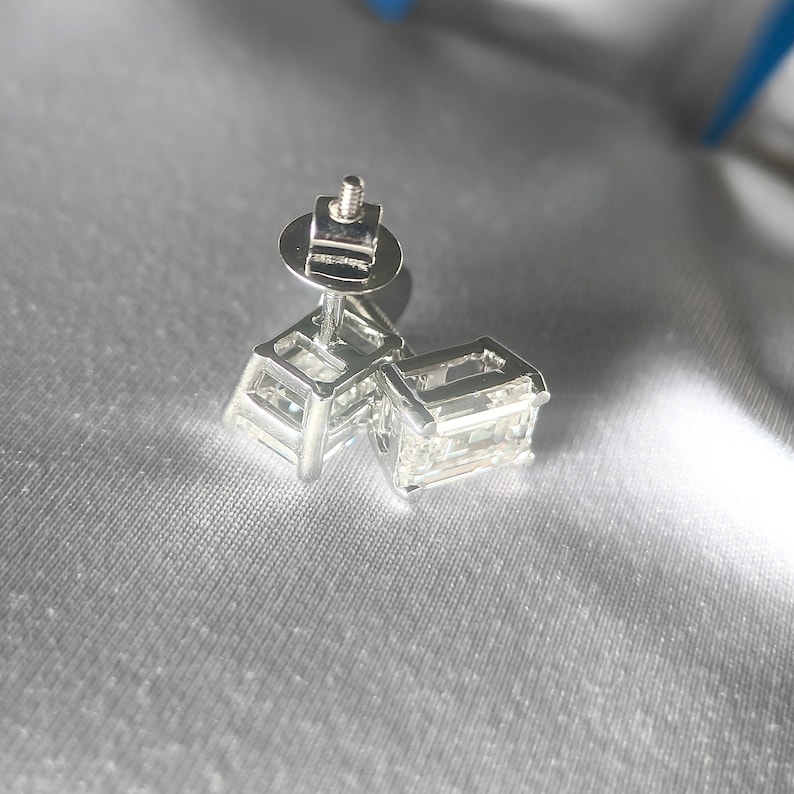K&ouml;nnte beinhalten: Ein Paar silberne Ohrringe mit einem quadratischen Diamanten in jedem Ohrring.