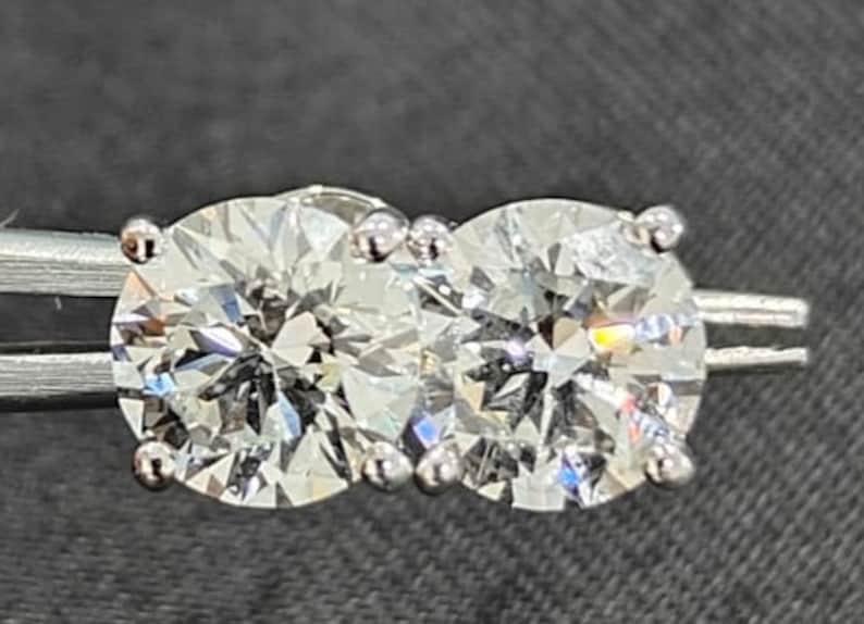 May include: Two round, clear, sparkling diamonds set in a silver band. The diamonds are set close together and are surrounded by small, silver prongs.