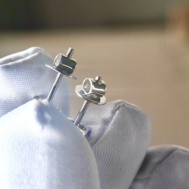 K&ouml;nnte beinhalten: Ein Paar silberne Ohrstecker mit Schraubverschluss. Die Ohrringe liegen auf einer wei&szlig;en Oberfl&auml;che.
