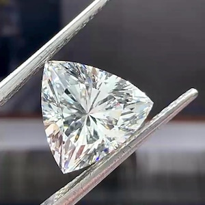 Pu&ograve; includere: Un diamante a taglio triangolare, tenuto da pinzette d'argento. La gemma brilla con numerose sfaccettature che riflettono la luce. La forma del diamante &egrave; un triangolo equilatero, che ne evidenzia la chiarezza.