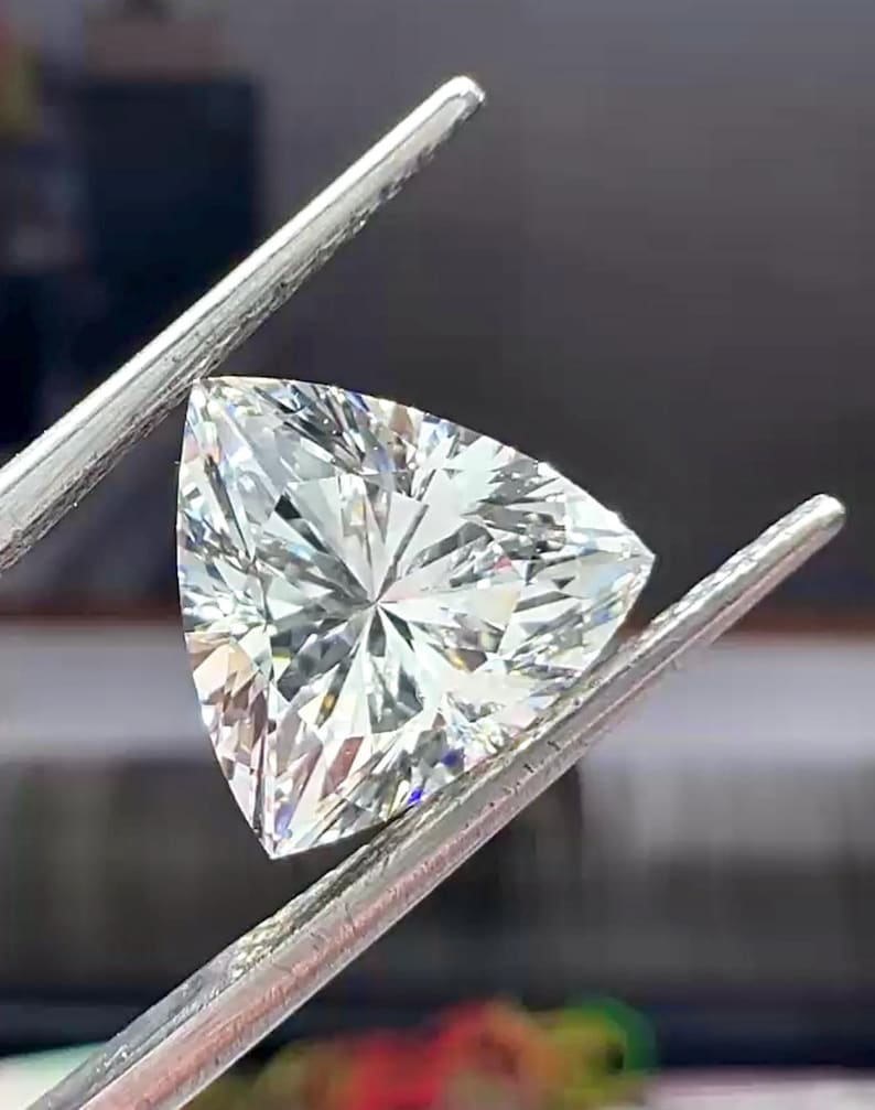 Pu&ograve; includere: Un diamante a taglio triangolare, tenuto da pinzette d'argento. La gemma brilla con numerose sfaccettature che riflettono la luce. La forma del diamante &egrave; un triangolo equilatero, che ne evidenzia la chiarezza.
