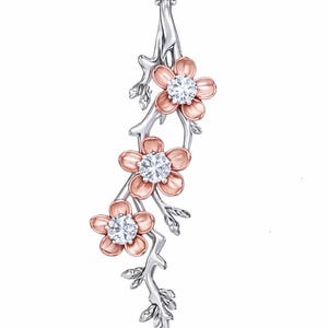 May include: A silver-tone pendant necklace featuring a floral design. The pendant has three flowers with pink petals and a sparkling, round, clear gemstone center. The flowers are attached to a silver-tone branch with leaves.