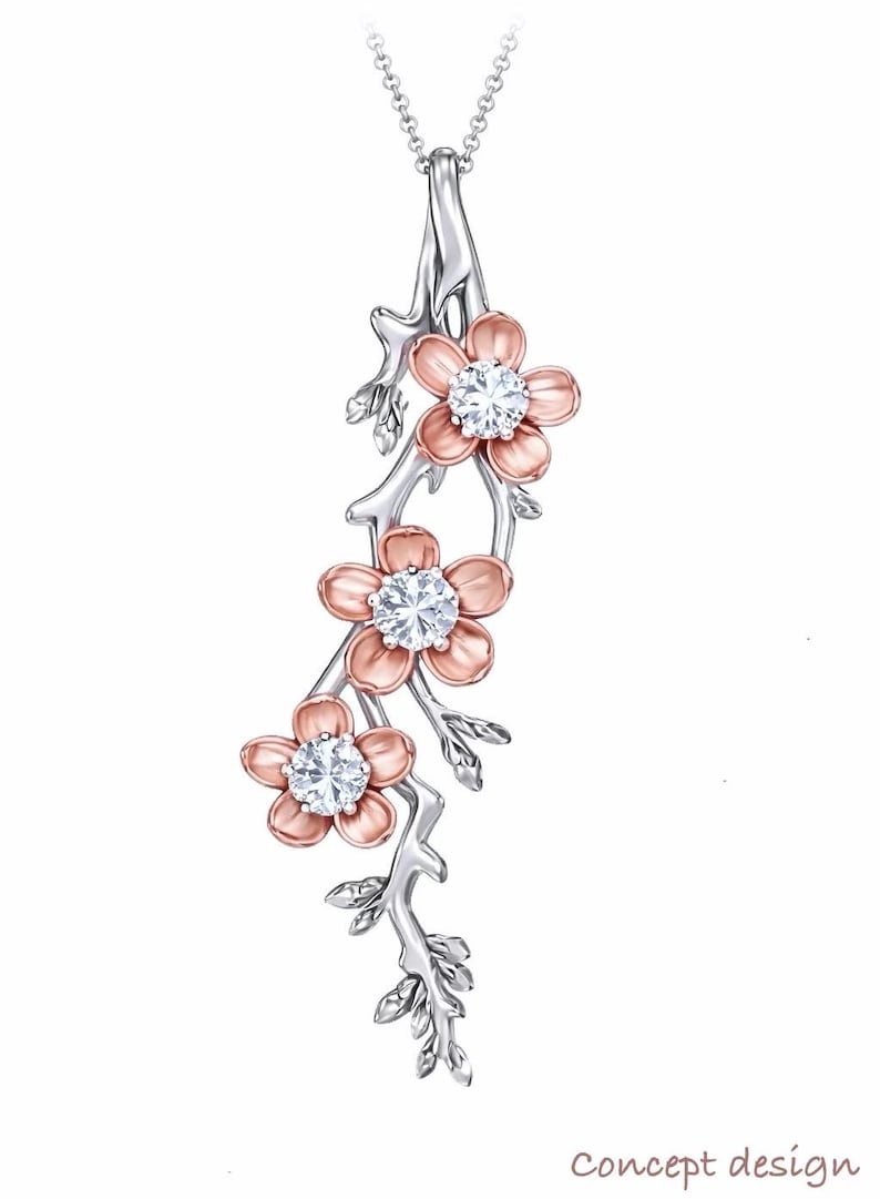 May include: A silver-tone pendant necklace featuring a floral design. The pendant has three flowers with pink petals and a sparkling, round, clear gemstone center. The flowers are attached to a silver-tone branch with leaves.