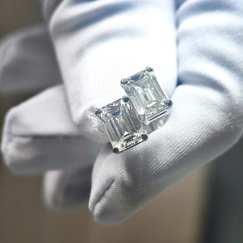 May include: Two emerald cut diamond earrings with a white gold setting.