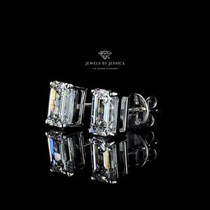 K&ouml;nnte beinhalten: Ein Paar Smaragdschliff-Diamant-Ohrringe, die in einer silbernen Fassung gefasst sind. Die Ohrringe befinden sich auf einem schwarzen Hintergrund.