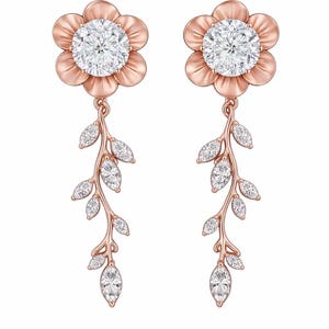 May include: A pair of rose gold earrings. Each earring features a flower-shaped top with a large, round, clear stone center. Below, a delicate vine with marquise-cut stones and leaf details hangs gracefully. The text "Concept design" is at the bottom.