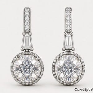 May include: A pair of silver drop earrings. Each earring has a large, round, clear gemstone encircled by smaller stones. The design includes a baguette-cut stone and a row of small stones at the top. The words "Concept design" are at the bottom.