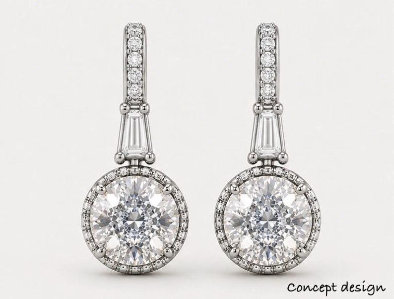 May include: A pair of silver drop earrings. Each earring has a large, round, clear gemstone encircled by smaller stones. The design includes a baguette-cut stone and a row of small stones at the top. The words "Concept design" are at the bottom.
