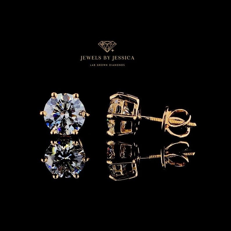 May include: Two gold stud earrings with round, clear lab grown diamonds. The earrings are set against a black background. The text 'Jewels by Jessica Lab Grown Diamonds' is displayed above the earrings.