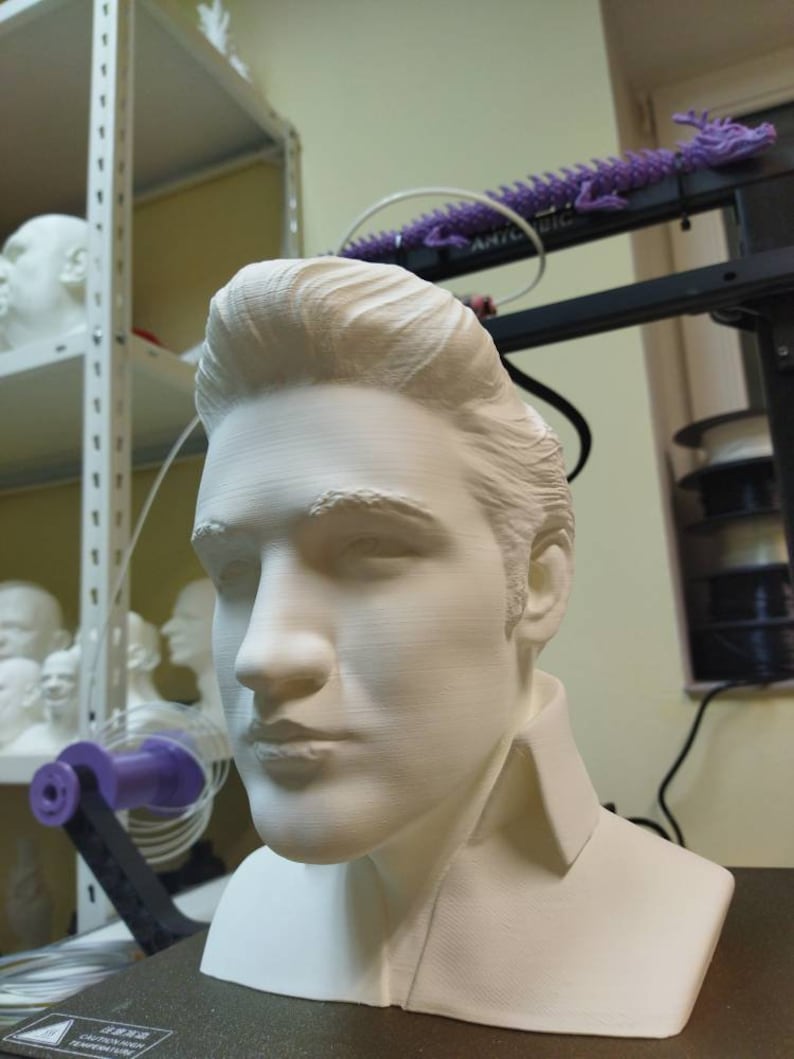 May include: A white 3D printed bust of a person with short, styled hair. The bust is on a black surface.