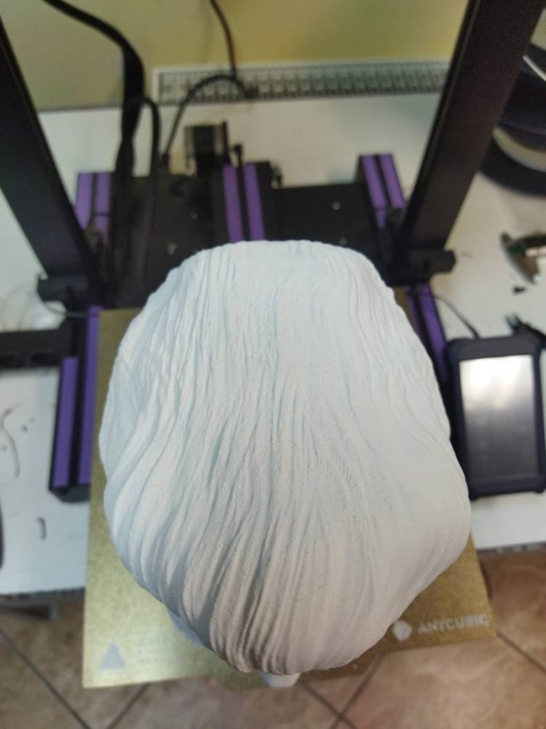 May include: A white 3D printed bust of a person with a textured surface. The bust is sitting on a gold surface with a black and white triangle logo.