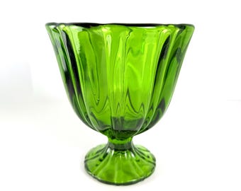 May include: A green glass footed bowl with a fluted design. The bowl has a wide, open top and a rounded base. The glass is a vibrant green color and appears to be vintage.